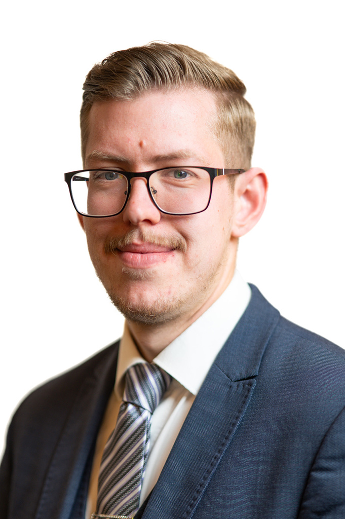 Mann mit Brille lächelt leicht, trägt Anzug und gestreifte Krawatte, hellbraunes Haar.