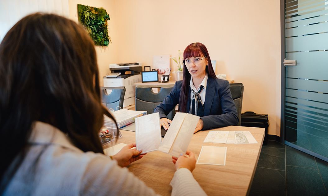 Eine Frau mit rotem Haar und Brille berät freundlich eine Kundin im Büro