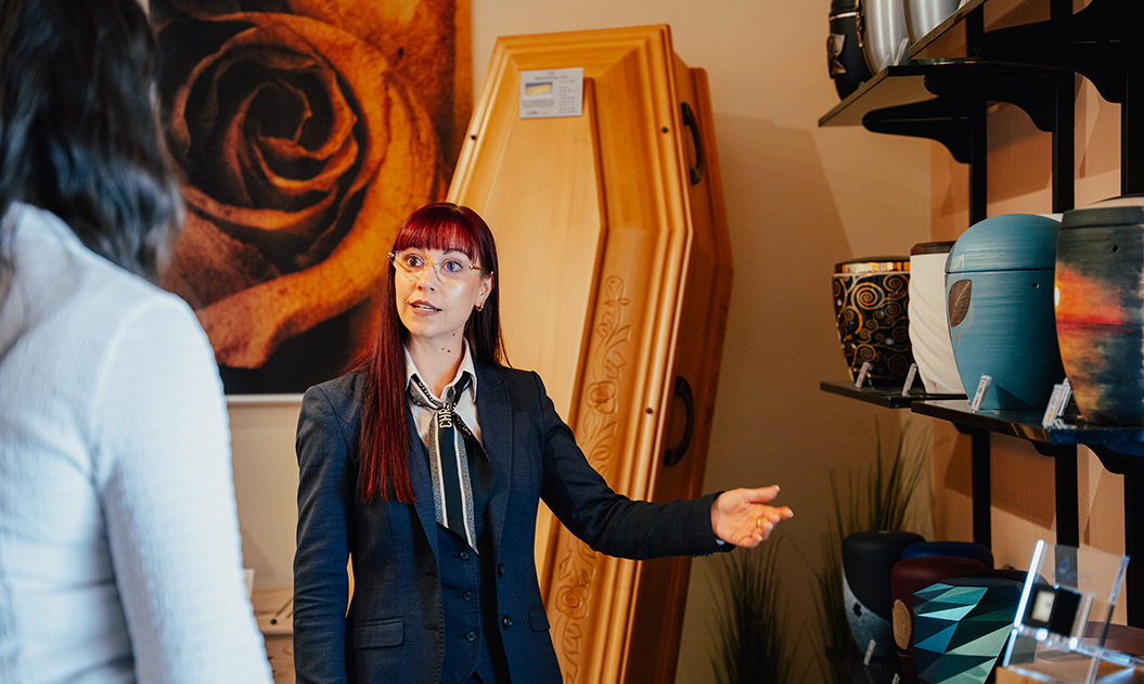Frau mit roten Haaren und Brille erklärt freundlich Urnen und einen Holzsarg