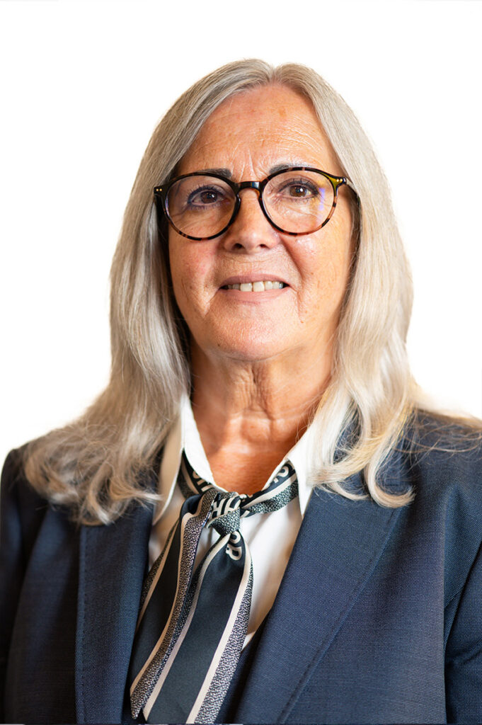 Eine ältere Frau mit grauem Haar, Brille und freundlichem Lächeln im Blazer