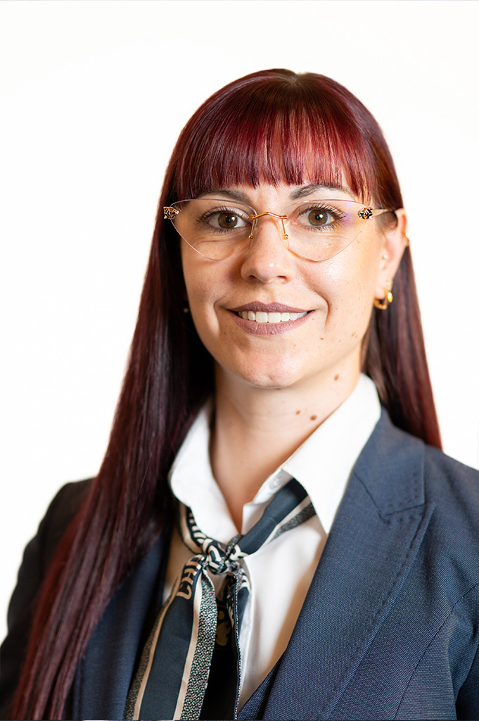 Frau mit langen roten Haaren, Brille und freundlichem Gesichtsausdruck im Anzug