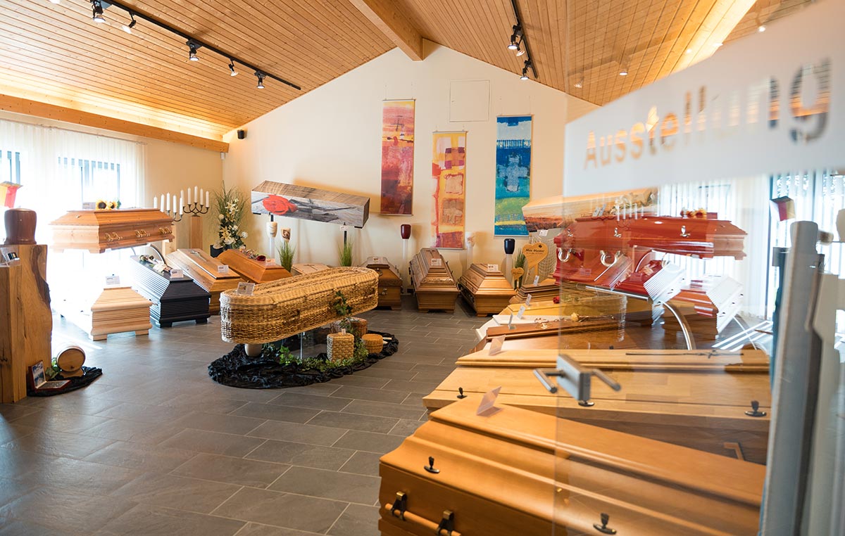 Mehrere unterschiedlich gestaltete Särge stehen in einem hellen Ausstellungsraum